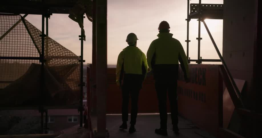 Two men wearing hard hats talk at a construction site