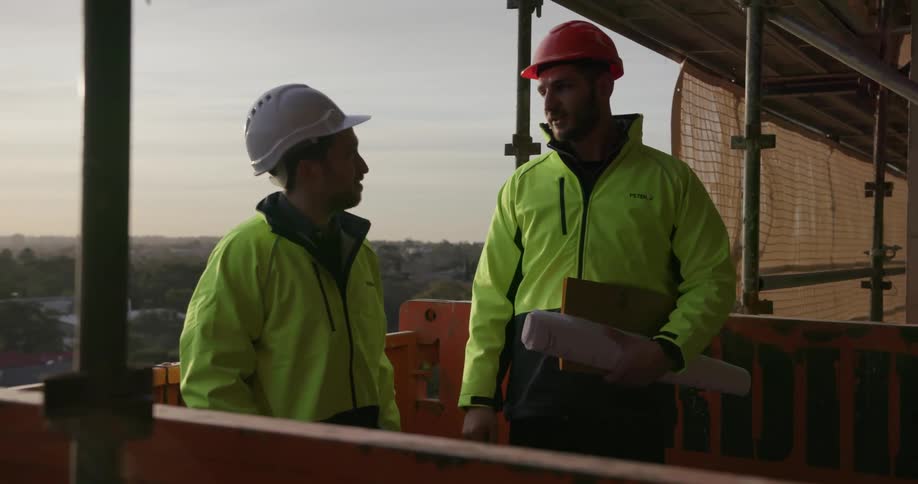 Two men wearing hard hats discuss a building site
