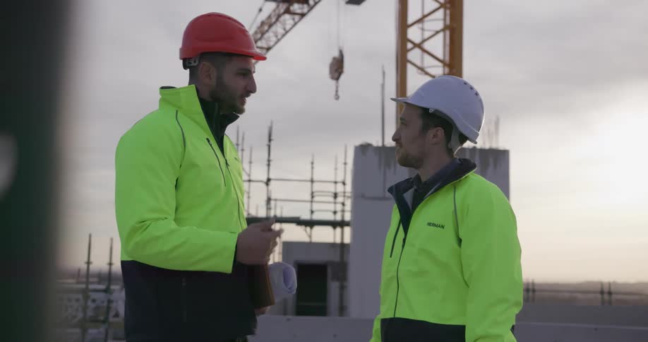 Two construction workers have a conversation in the cool evening air