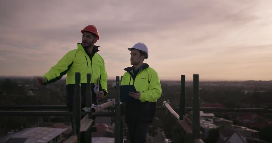 Two men in hard hats stand on the roof of building site