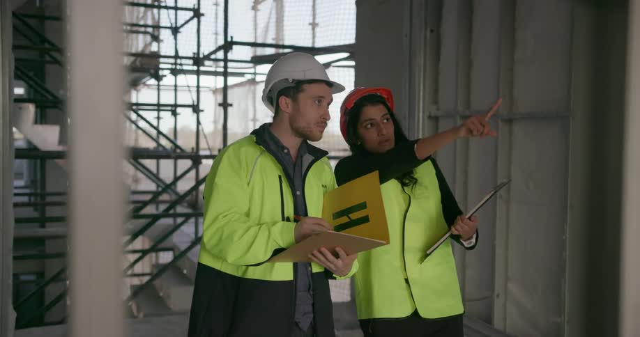 A man and woman in hard hats talk at a construction site