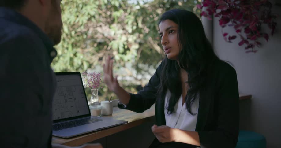 A woman and man sit by the window of the shop looking at a laptop and talking