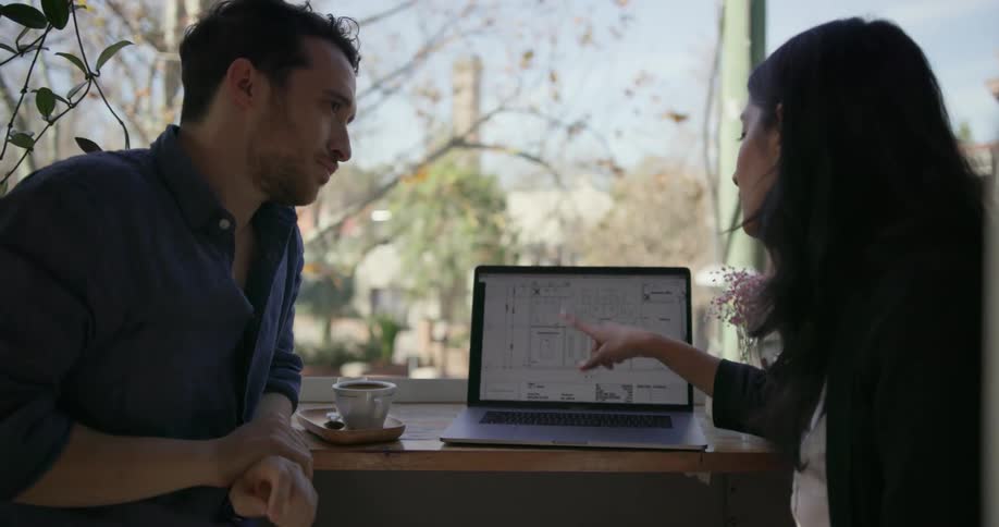 A man and woman have a conversation by an open laptop