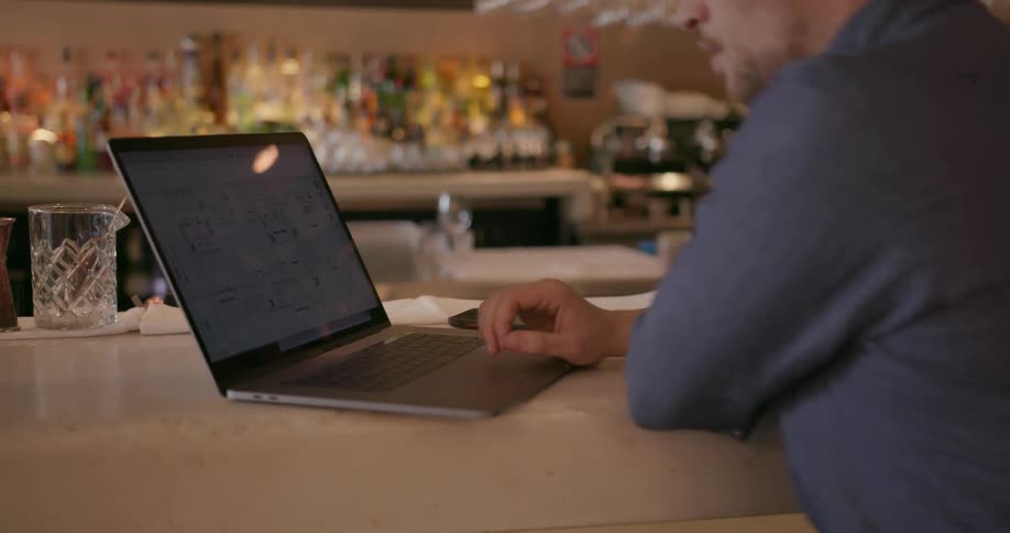 A man leans forward to use his laptop in a restaurant