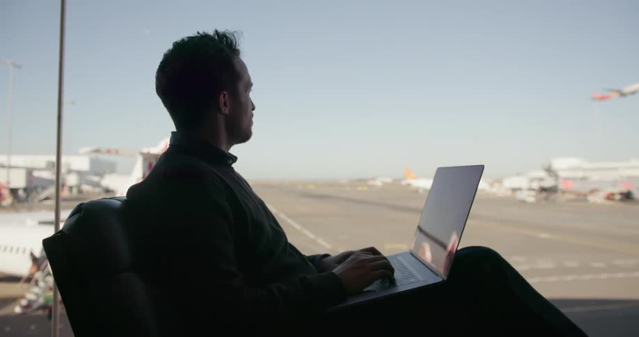 Man sits in an airport and types on his laptop
