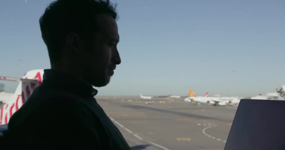 A man sitting in an airport watches a plane take off
