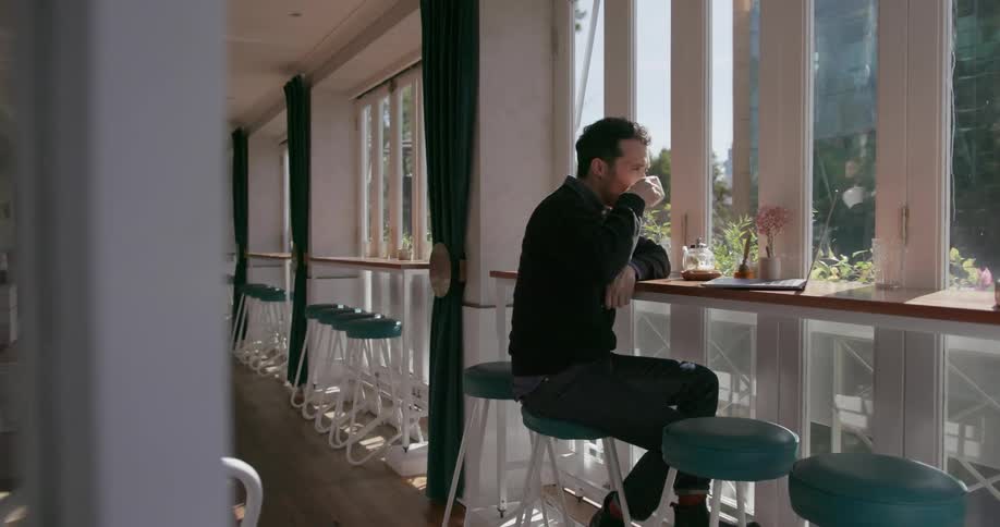 A man is sitting by the window using his laptop