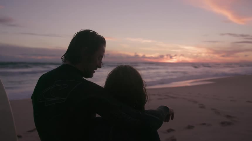 A man points out the sunset to a woman while on the beach