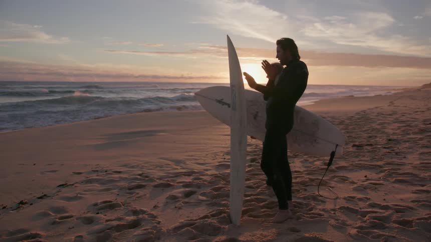 Man and woman holding surfboards stand talking on the beach