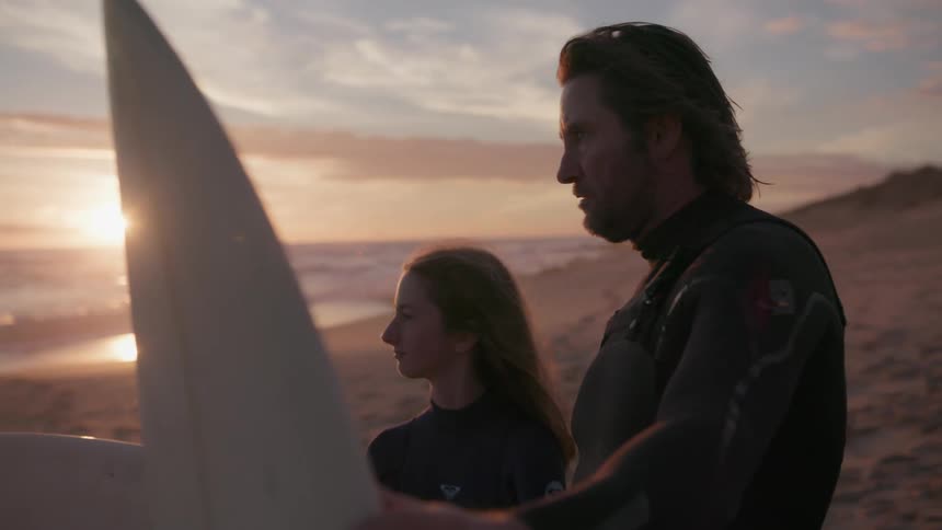 A man and woman talk with surfboards on the beach