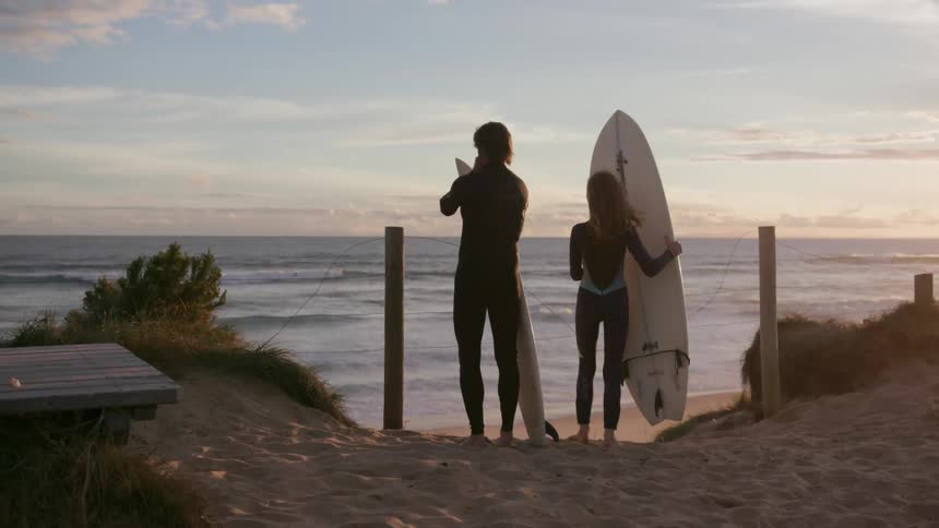 A man and a woman approaching the water holding surfboards