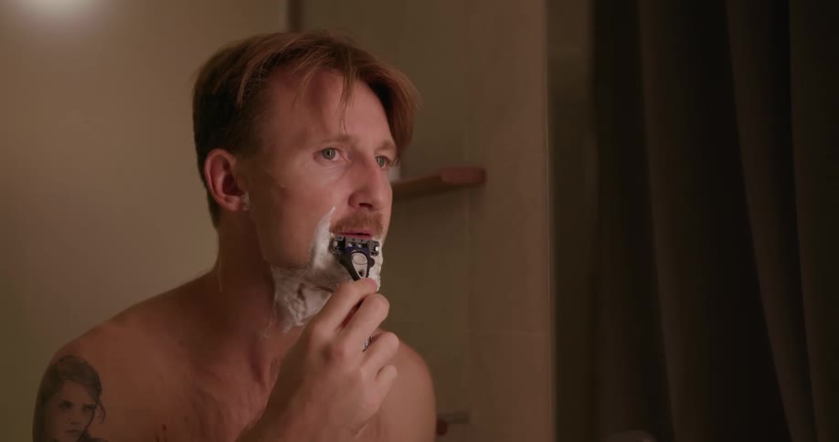 A man shaves his face in a mirror