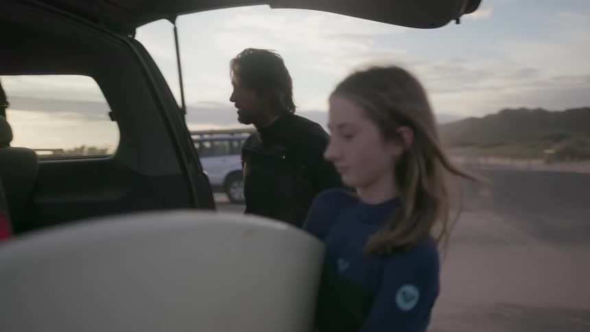 A man walks over to a truck and removes a surfboard