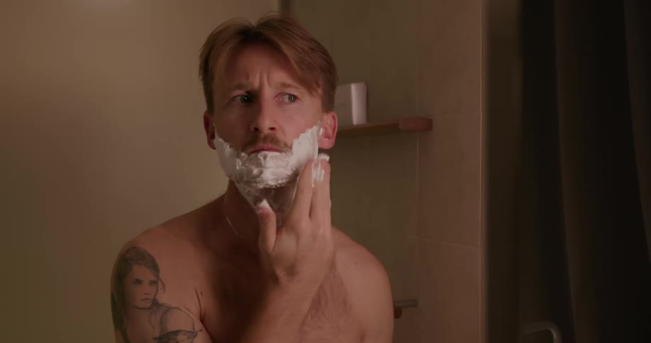 A man standing in a bathroom is applying shaving cream to his face