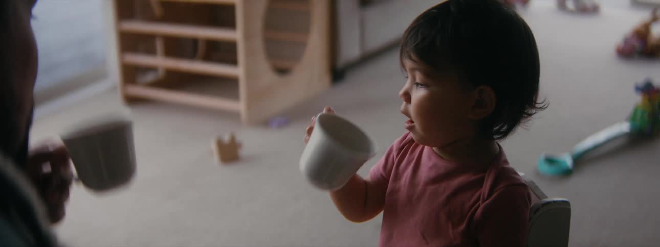 A child pretends to drink from an empty cup with an adult