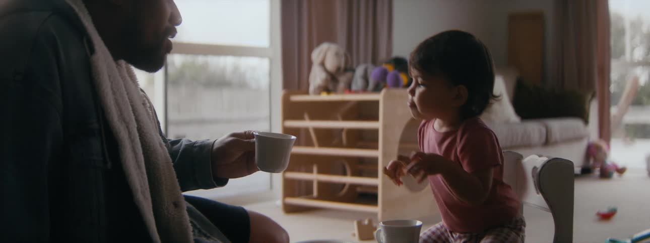 A young girl eats a cookie at a pretend tea party with her father