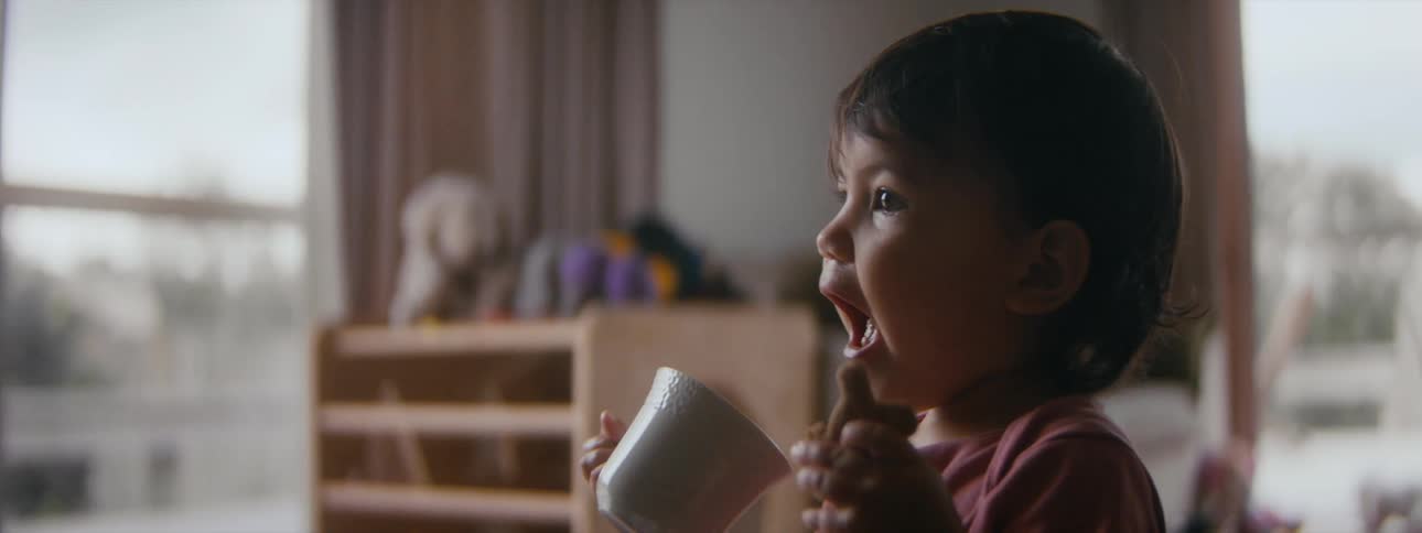 A little girl pretends to drink out of a cup while playing at home