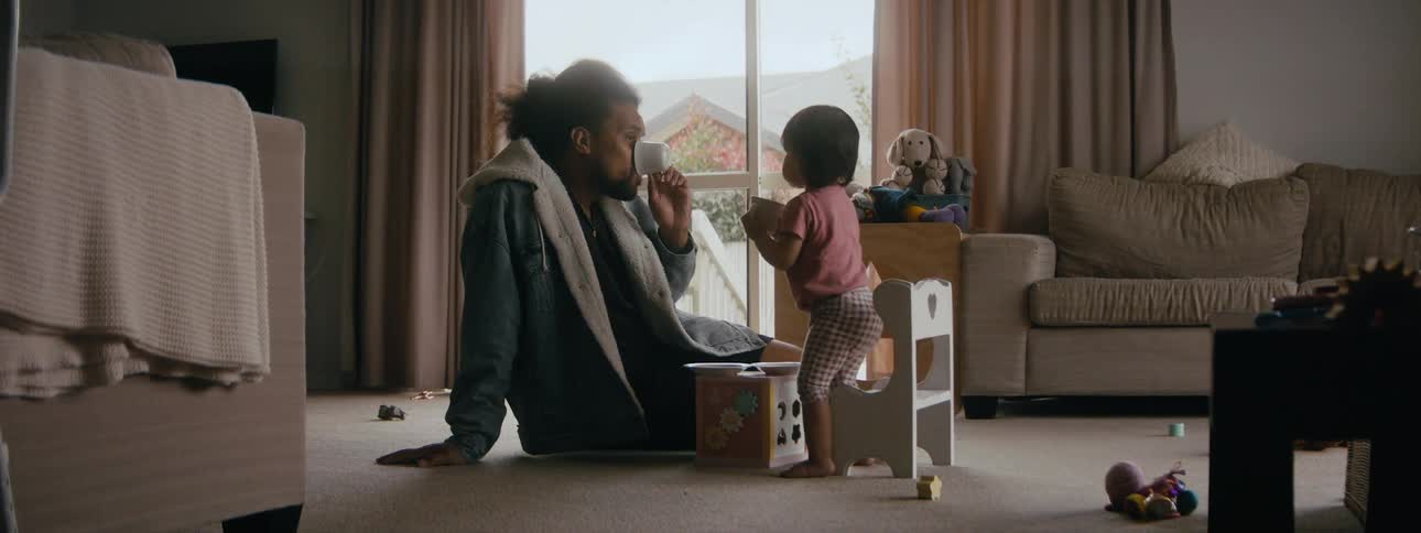 A man and a young girl pretend to drink from cups while holding a tea party on the floor of a living room of a house during the day
