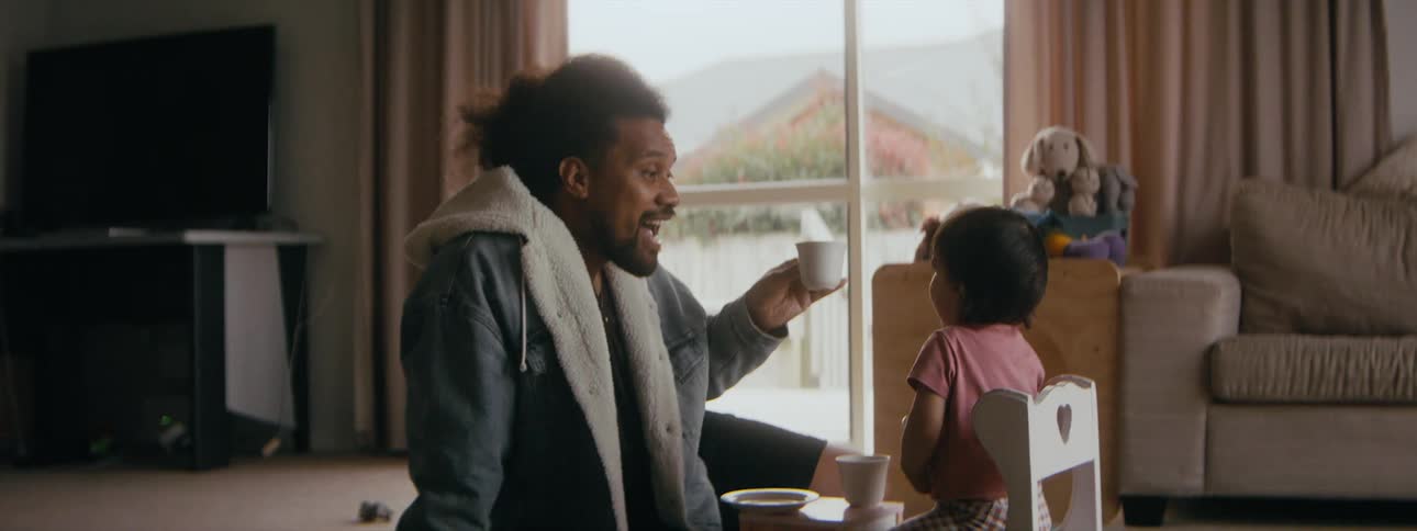 A father pretends to drink out of a cup while his daughter licks a plate while playing at home
