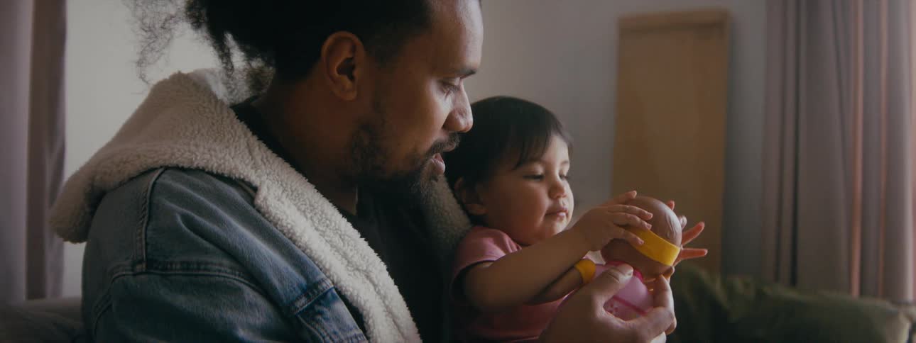 Dad sitting holding his daughter on his lap playfully makes the doll kiss her