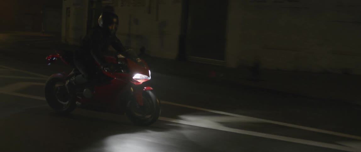 Two motorcycle riders travelling along a dark, city street