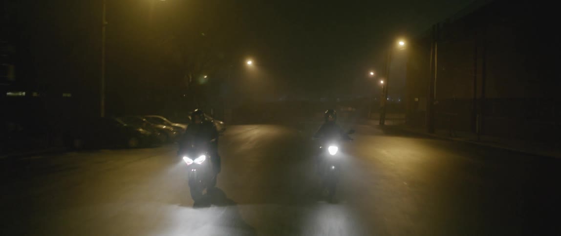 Two motorcycles drive down the street at night