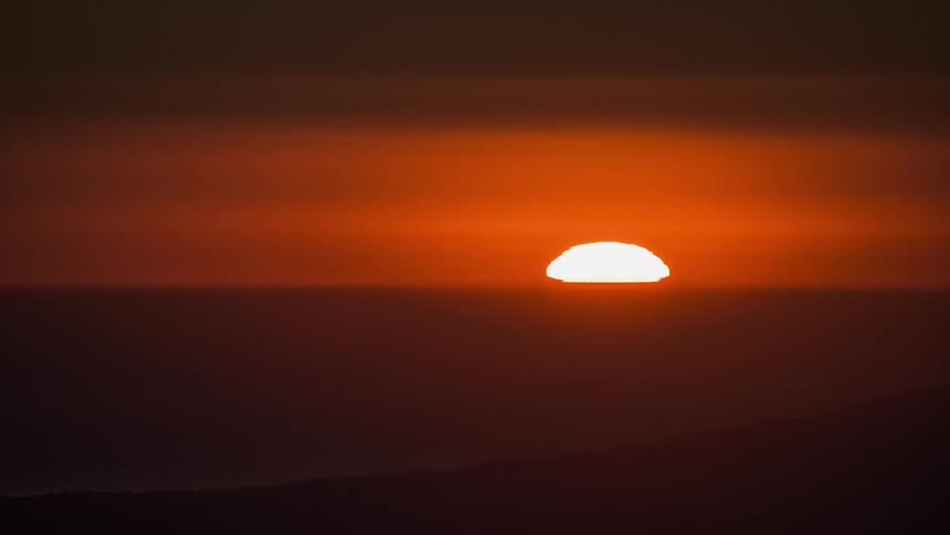 A glowing sun in an orange sky sets at the horizon