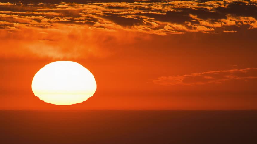 The sun sets over the ocean in a bright red and orange sky