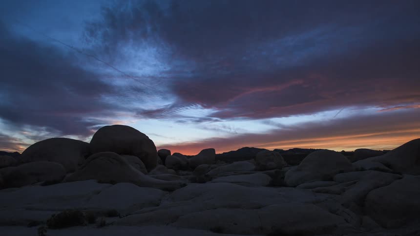 Clouds move over rocks in the desert as darkness falls