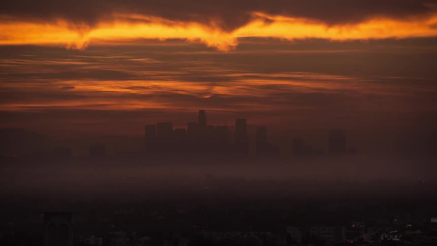 Sun rises turning sky a bright orange over silhouette of city skyline