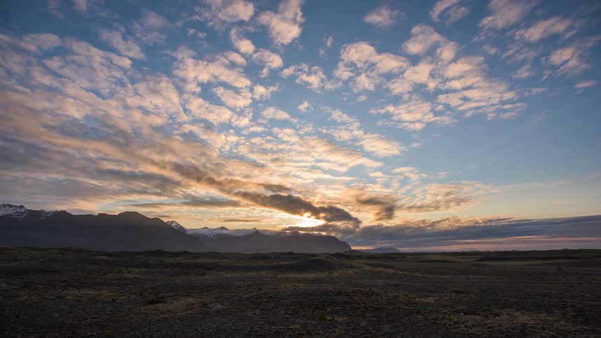 Clouds pass over flat lands with a mountain ridge on the horizon at sunrise