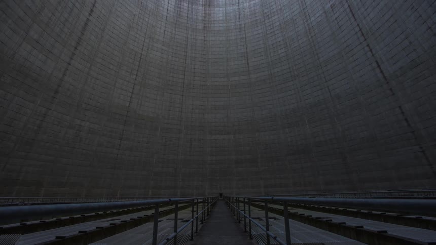 A timelapse shot of the rounded walls of a nuclear cooling tower leading up to the round opening showing sky and clouds