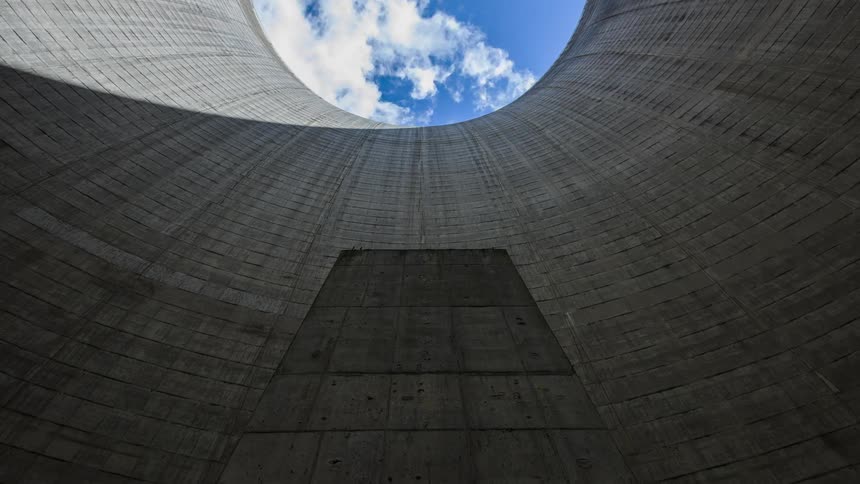 View looking up from the inside of a nuclear cooling tower as the clouds are moving across a blue sky