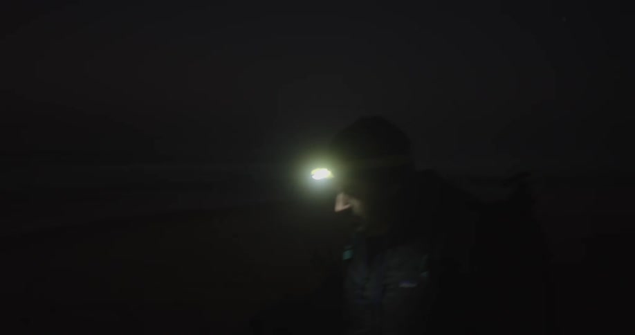 A man hikes at night while wearing a headlamp