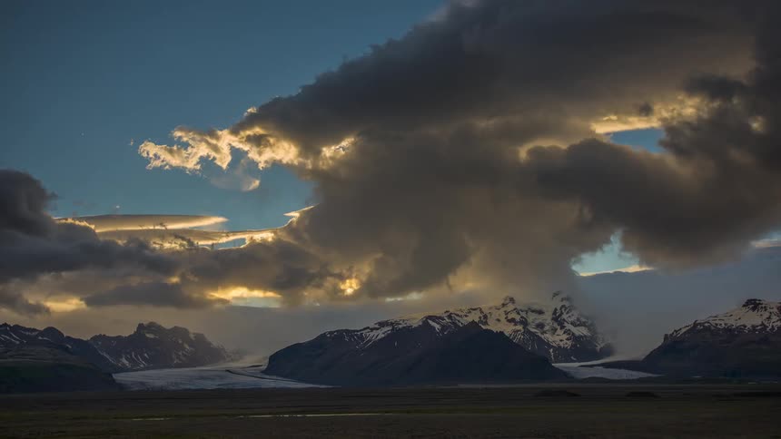Thick clouds gather and moving over snow capped rocky ridges along a river