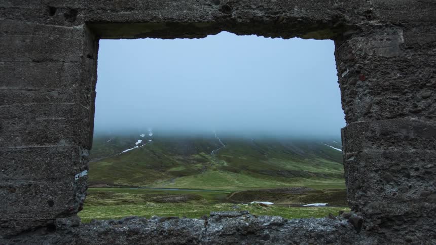View through the window in a stone wall of a foggy hillside and valley below