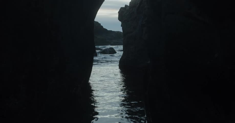 View from a sea cave of waves rolling in and splashing against rocks and ripples in the water