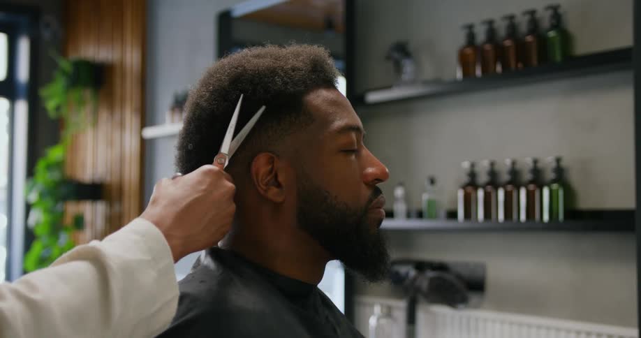 A man sits with a cape on as a woman trims his hair in a shop