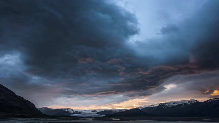 Sun rises on horizon over snow covered mountains and sea