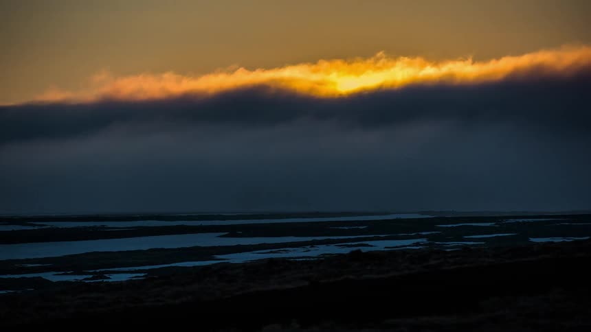 The sun sets behind thick rolling cloud cover making the sky gold before sinking