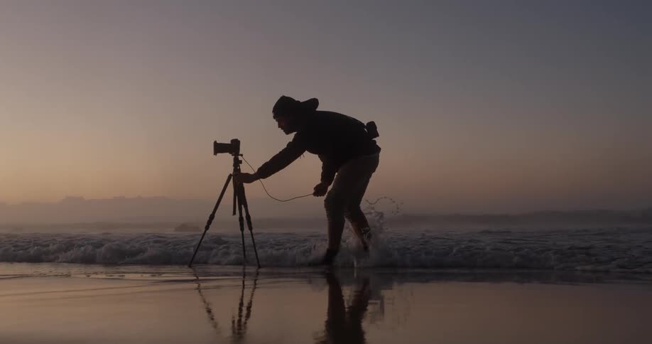 A man is setting up his camera on the beach
