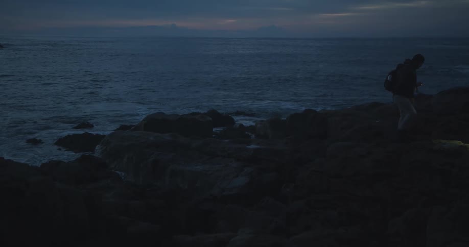 A man hikes up rocks along the coast at night
