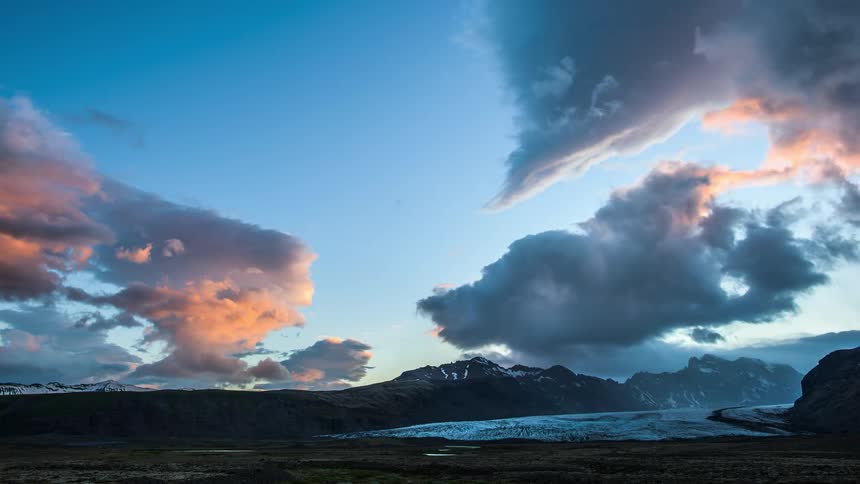 The sun shines on cumulus clouds moving over mountains