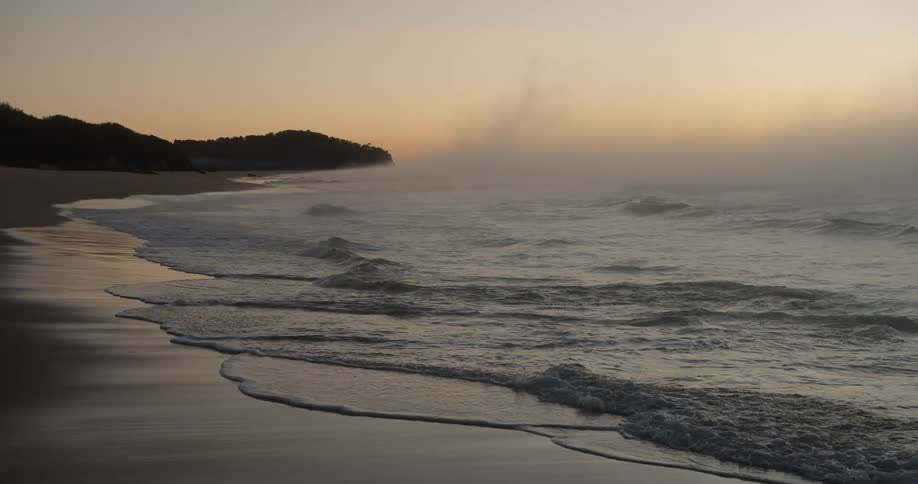 The tide washes into a sandy beach at sunset