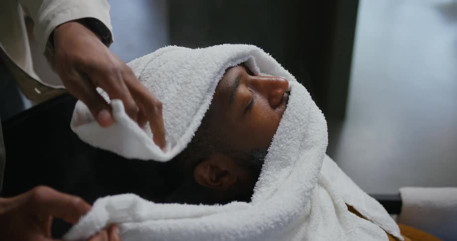 A barber puts a hot towel on a mans face