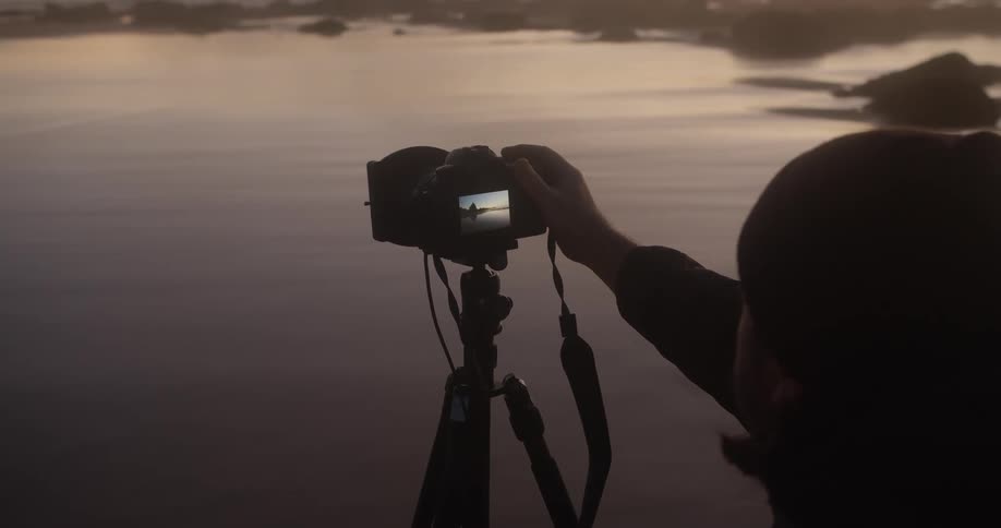 A person on the shore waits behind their camera for a large wave before taking a photo