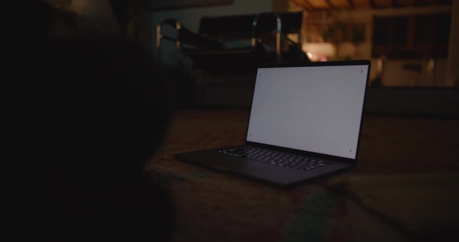 A man is sitting near a laptop computer on the floor with a white screen