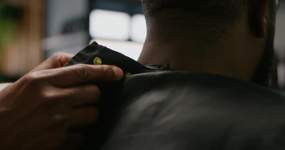 A barber secures a cape onto a client at a salon