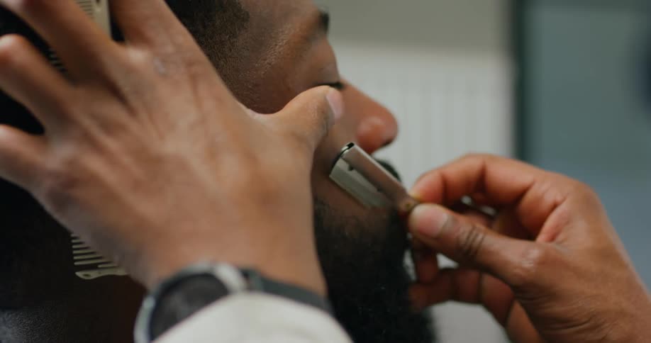 A barber is shaving a mans face with a razor