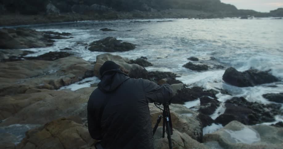 Male photographer with black beanie photographs the ocean